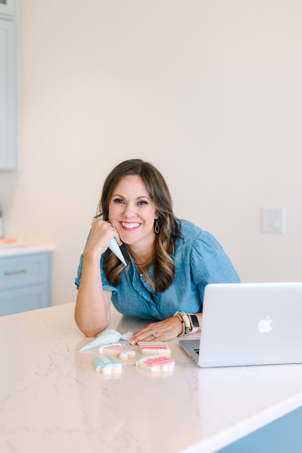 Branding portrait of a woman decorating cookies beside her laptop